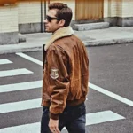 Vue de dos d'un homme en blouson bombardier cuir marron, traversant la rue, style pilote authentique.