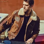 Homme avec un blouson cuir marron de style aviateur, col mouton, assis à l'intérieur d'une voiture vintage.