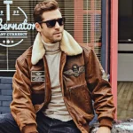 Homme assis sur une moto, portant une veste en cuir marron avec col fourrure, ambiance urbaine, vêtements homme.