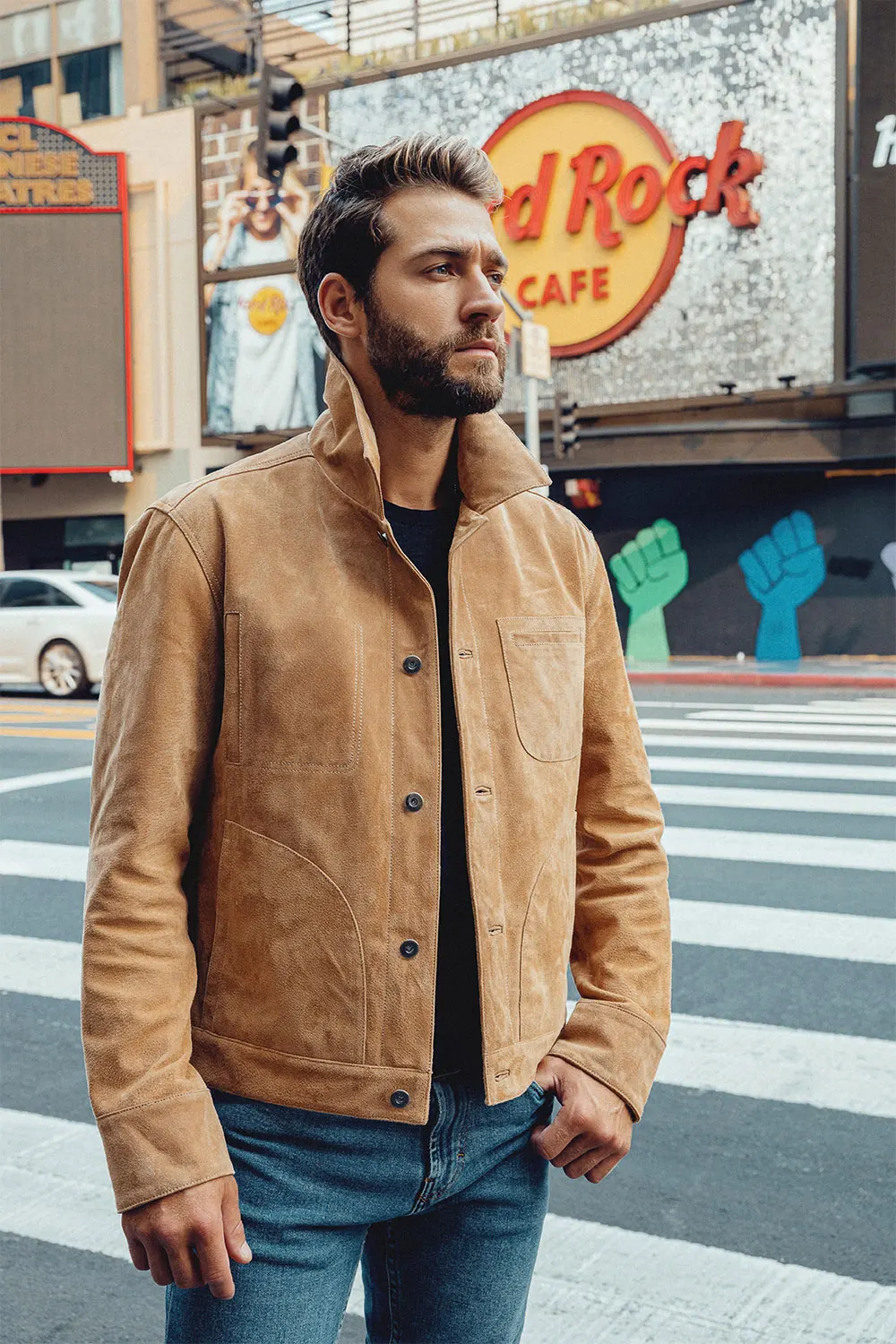 Modèle masculin posant avec un blouson en cuir marron clair, veste homme tendance avec fond urbain.