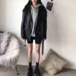 Femme portant un perfecto noir en cuir avec un sweat à capuche gris et un short cycliste, style urbain décontracté.