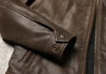Poignet de la veste en cuir marron avec boutons pression, détail du cuir et des coutures, finition soignée du blouson homme.